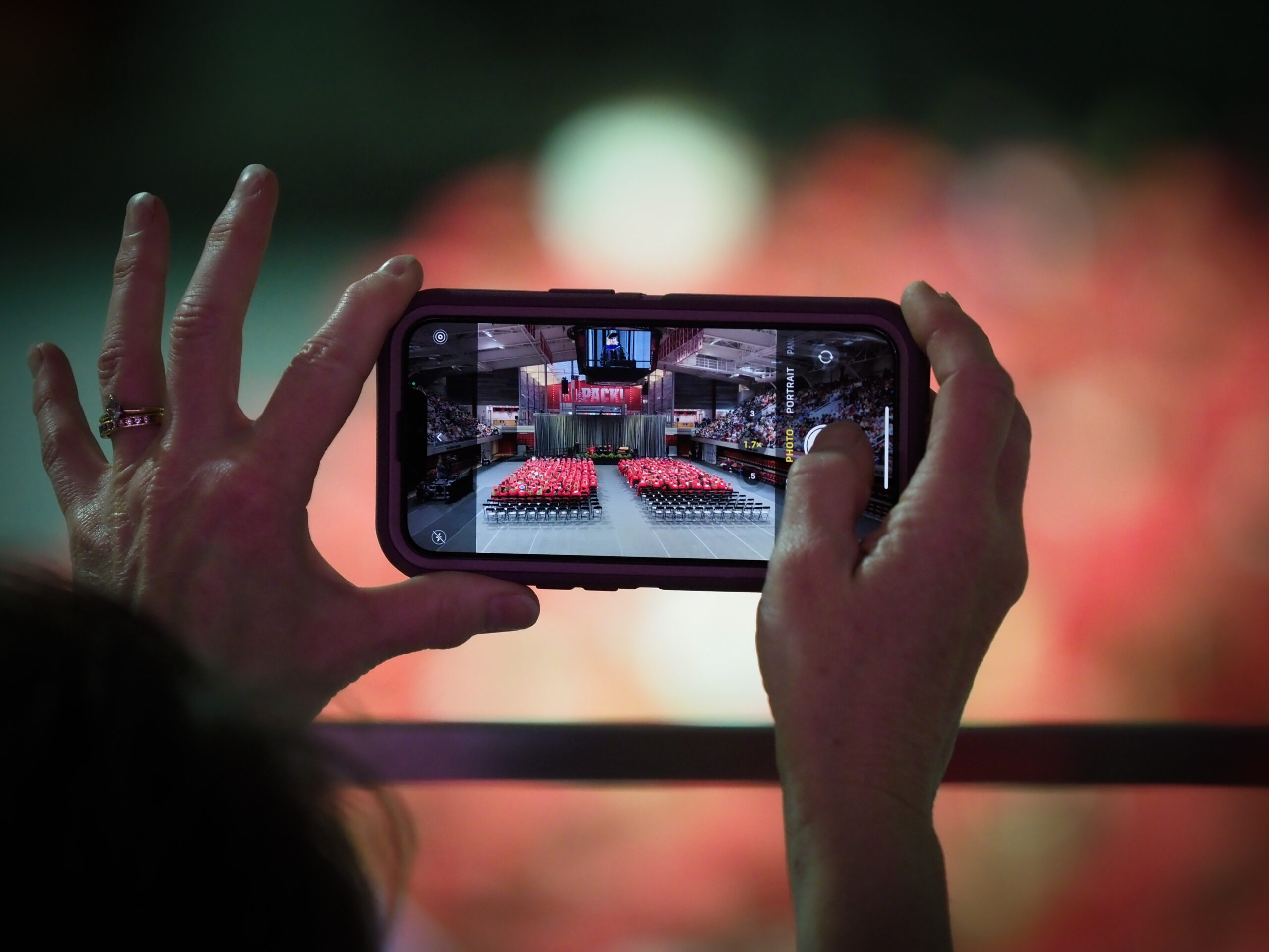 A closeup of hands taking a photo of an NC State graduation with a phone