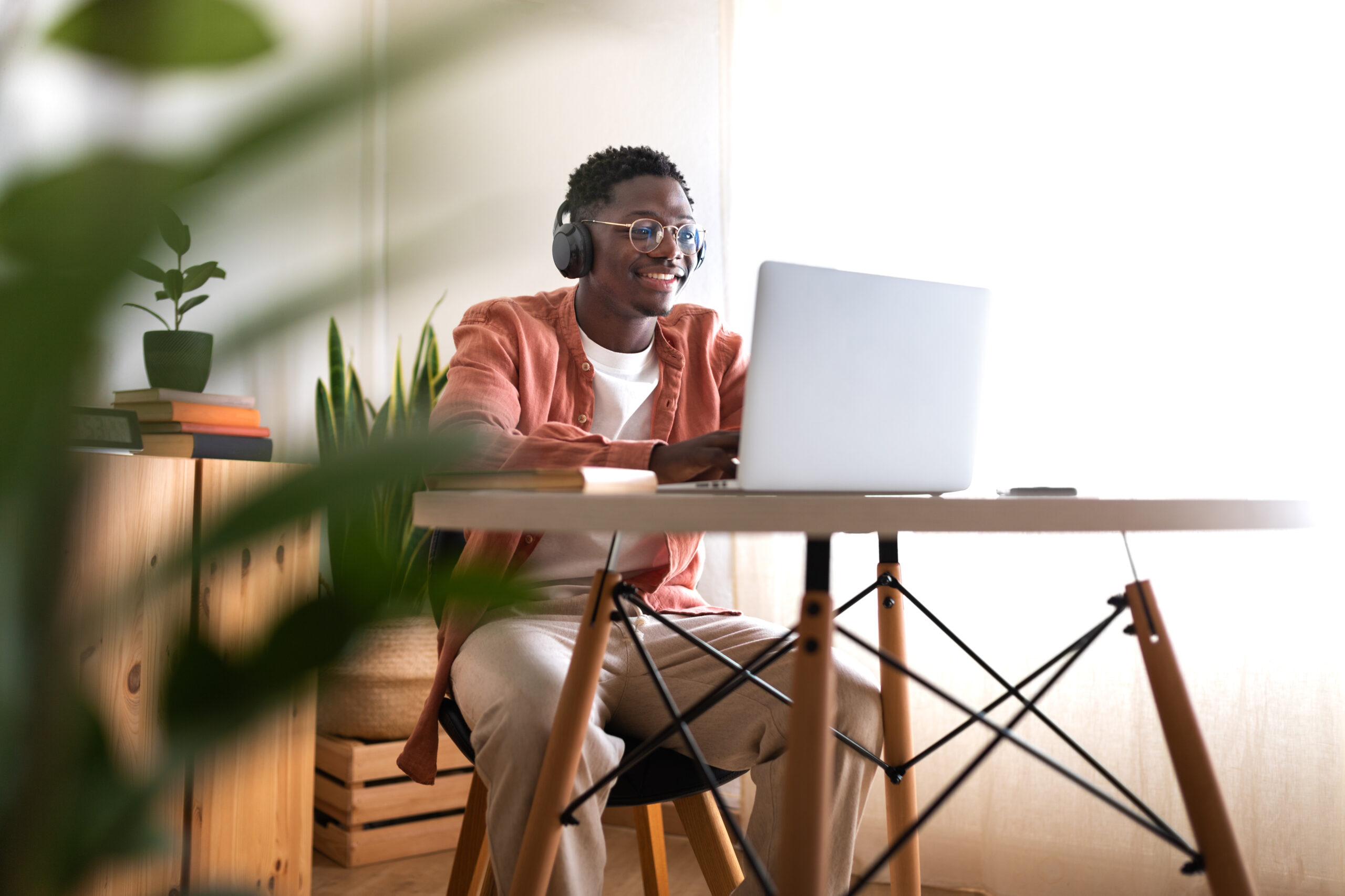 A man sits at a desk looking at a laptop and wearing headphones