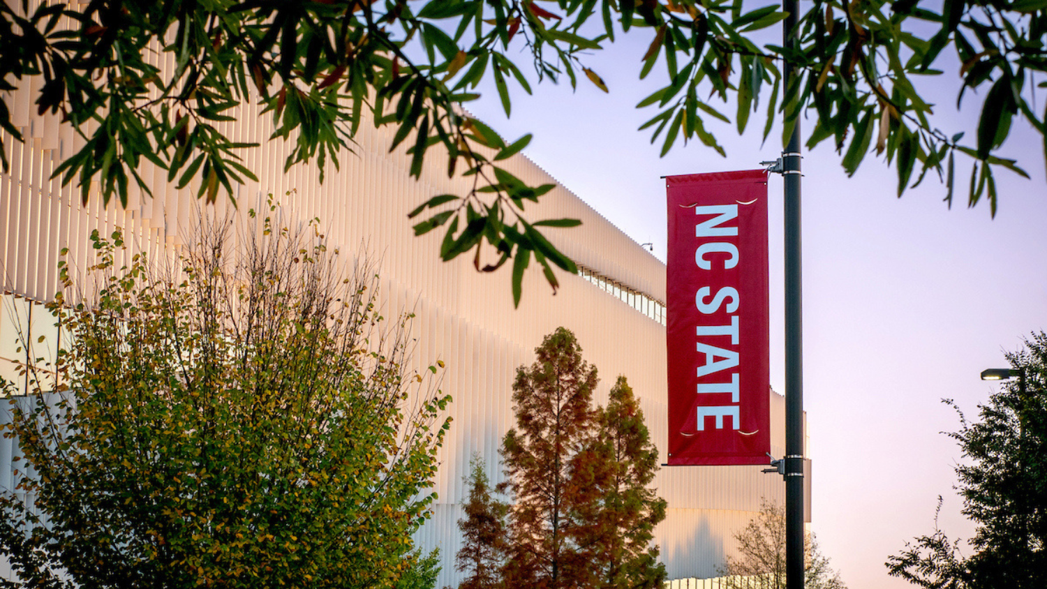 A red sign that says "NC State" hangs from a light pole on Centennial Campus