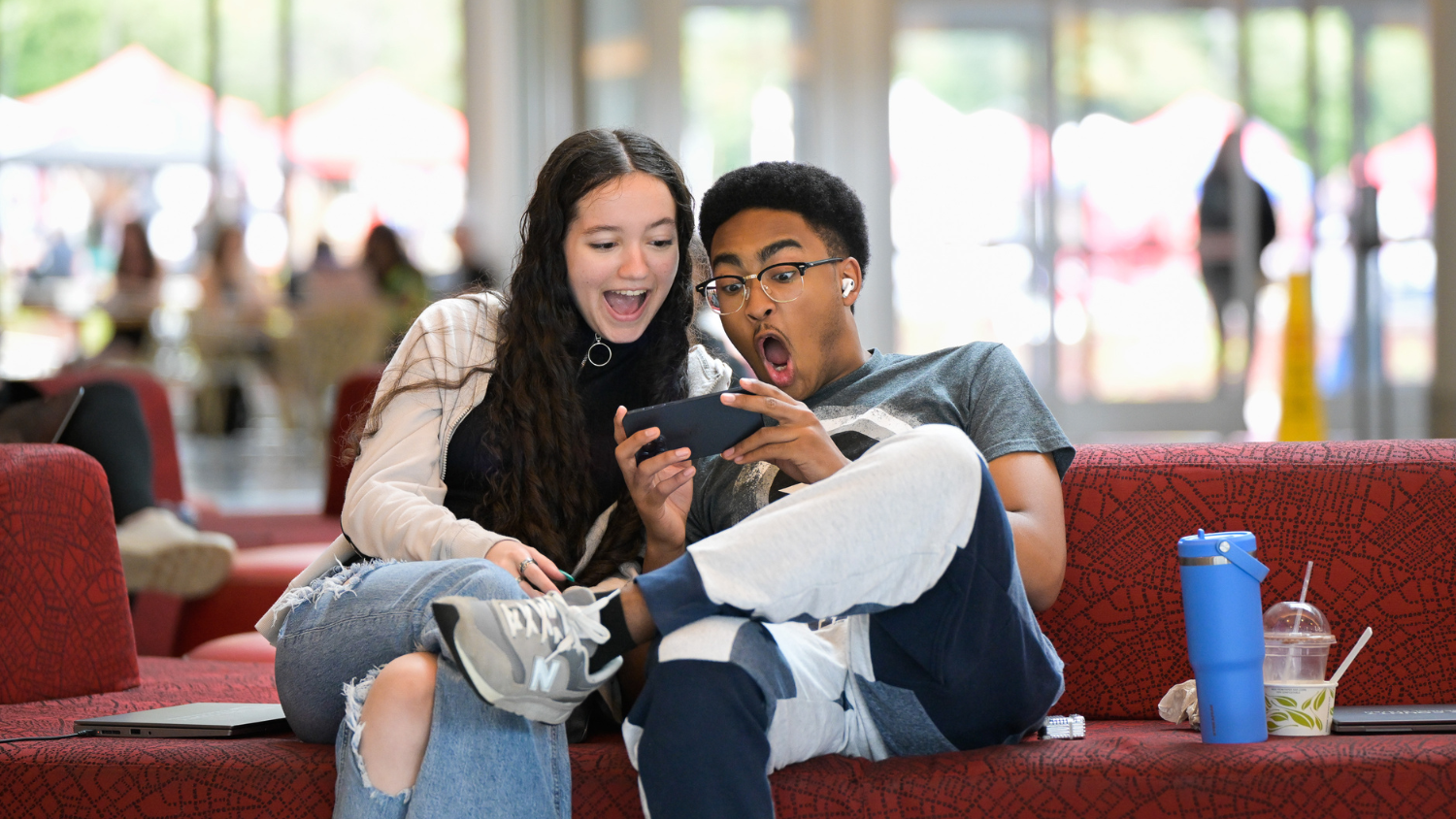 Two students look surprised while looking at a phone in Talley Student Union.