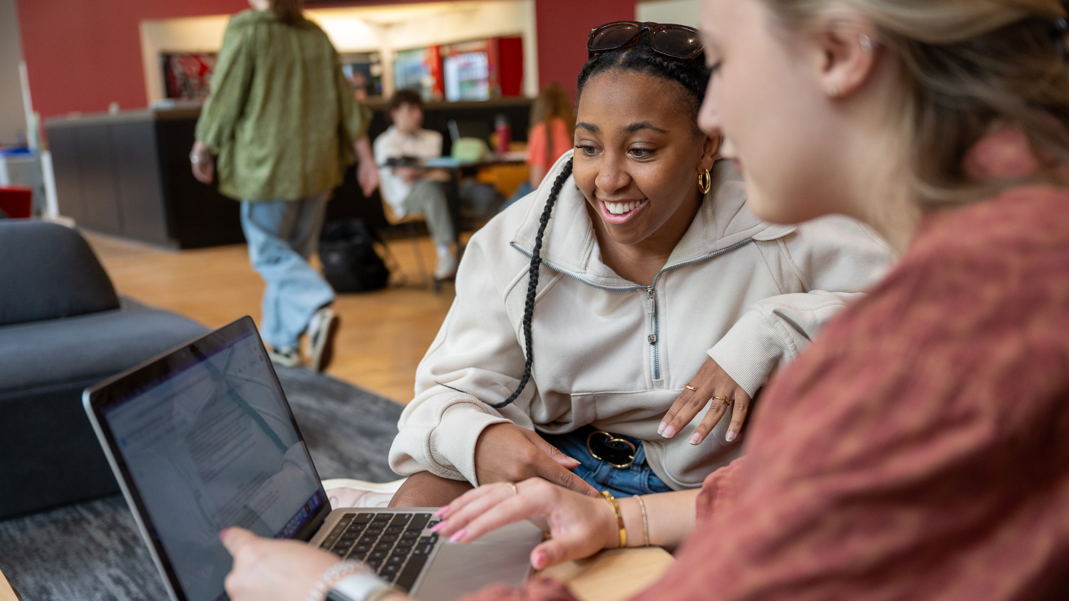 Two happy students look at a laptop together with one pointing at the laptop