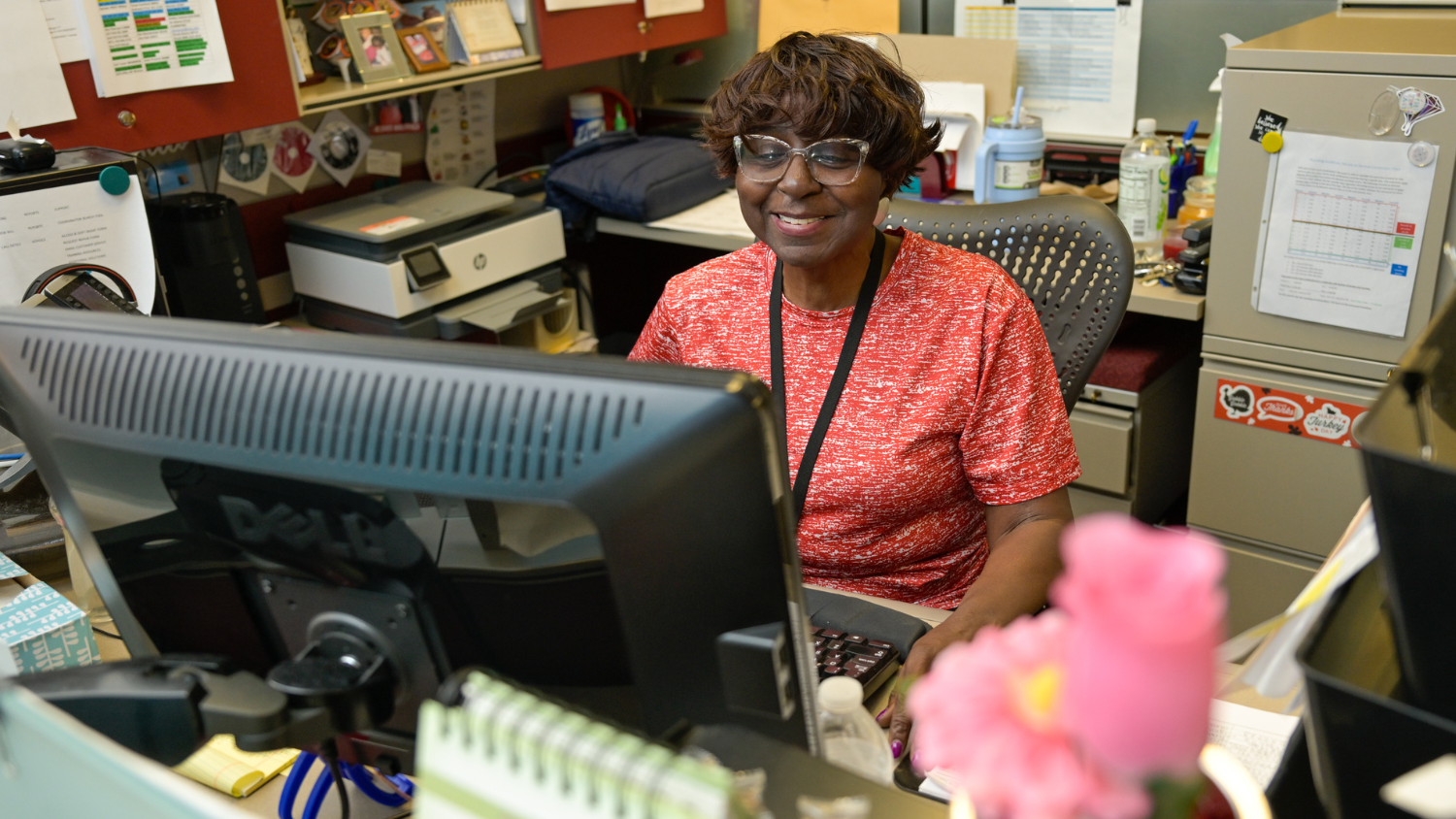 A staff members sits behind a computer monitor at a desk smiling.