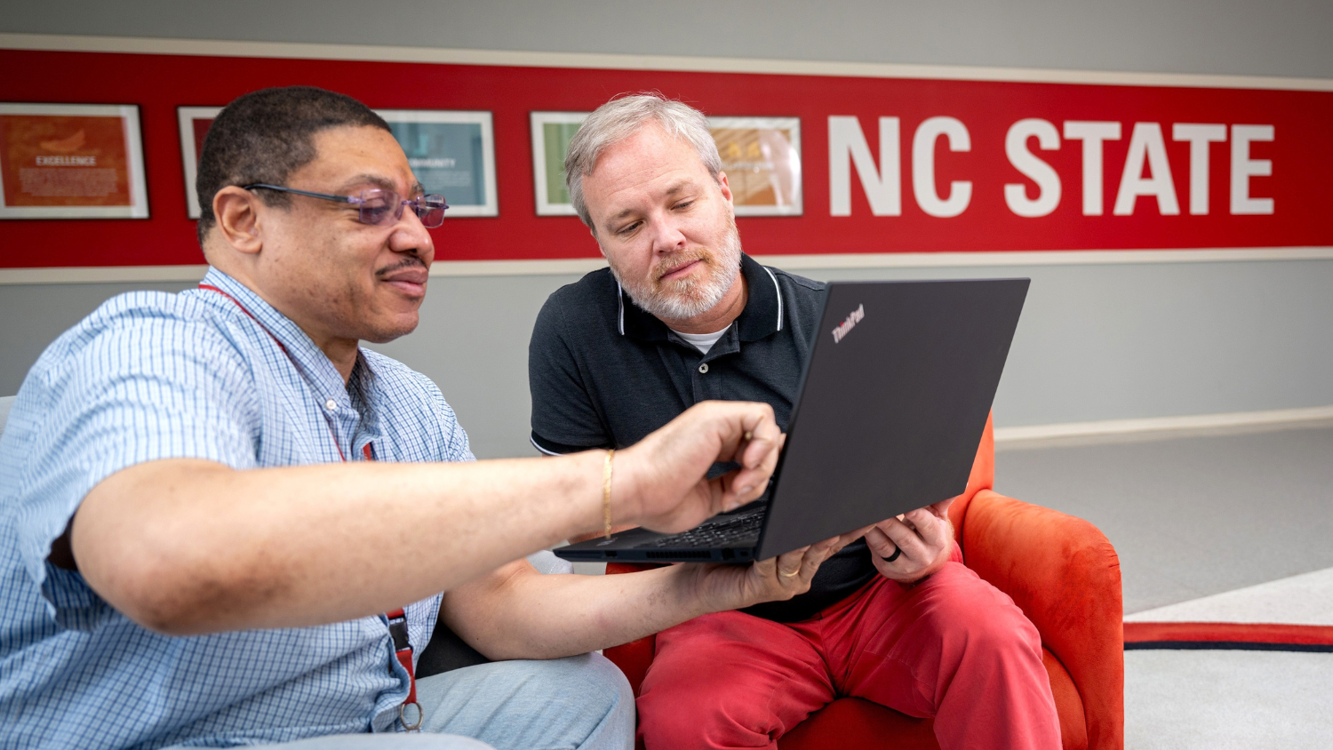 An IT staff member shows another employee something on laptop