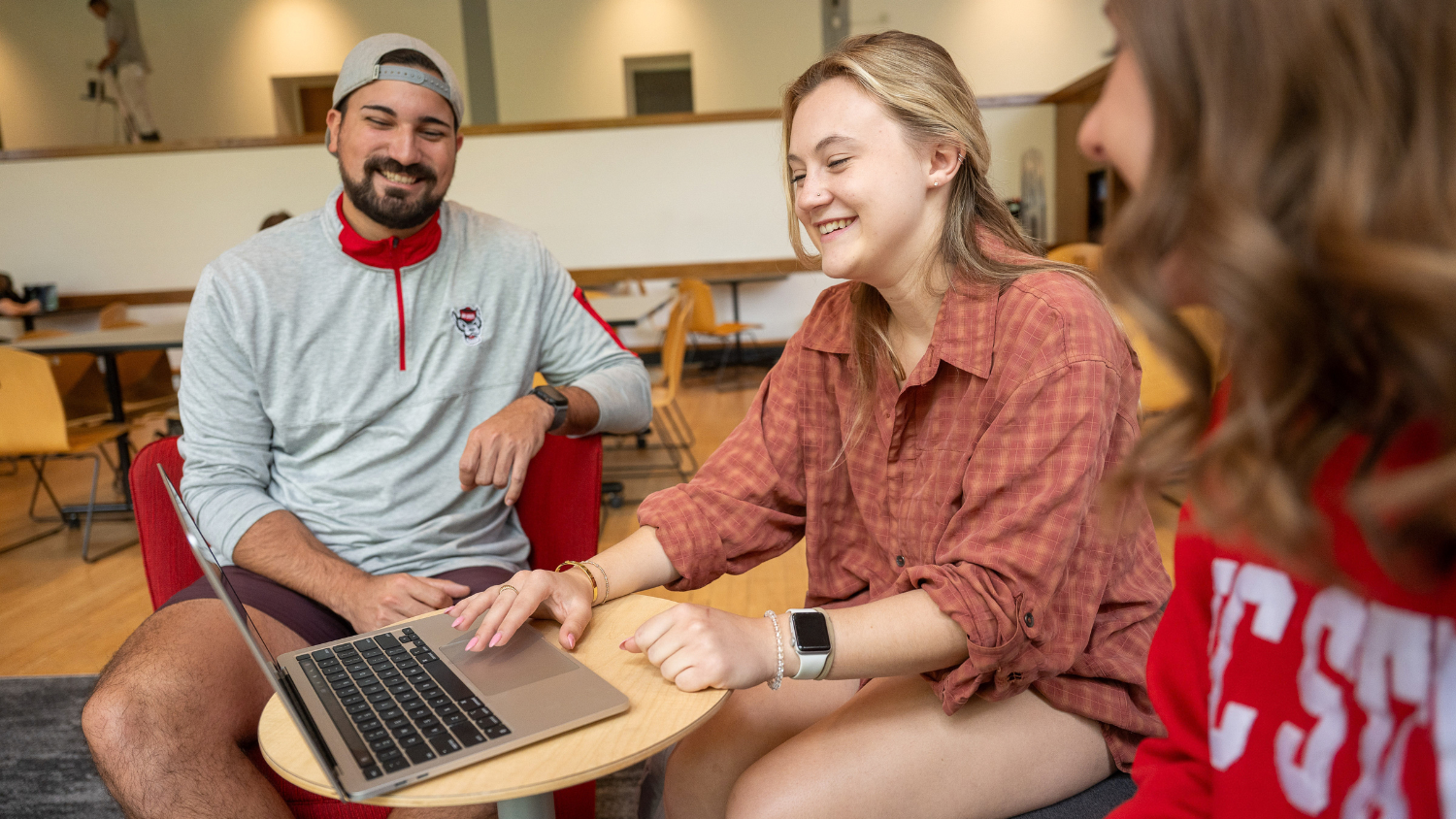 Three students smile and look at a laptop together