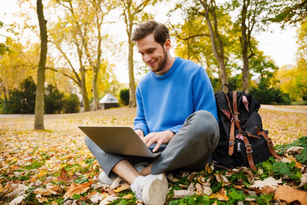 Person sit happily on autumn leaves while typing on a laptop